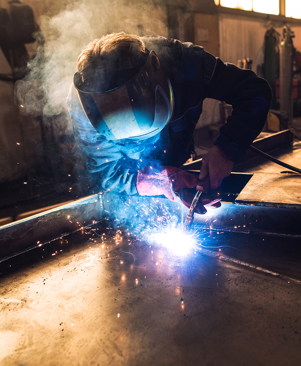 Professional welder in protective uniform and helmet welding met